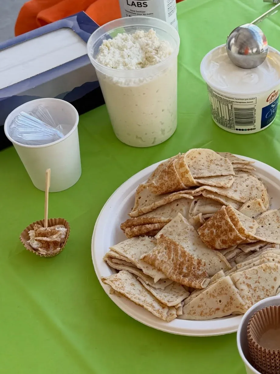 Folded crepes cut into triangles on a paper plate, with tubs of cottage cheese and sour cream, on a green tablecloth.